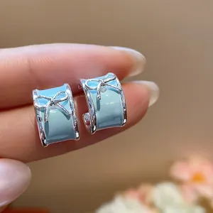 Macro view of light blue enamel C-shaped hoop earrings with silver bow details
