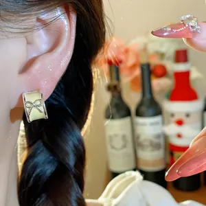 Close-up shot of a cream-colored oil-dripping bow C-shaped stud earring worn on an ear