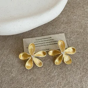 Detailed close-up of golden flower stud earrings with textured petals on a beige background.