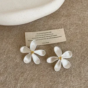 Detail shot of silver flower stud earrings with gold stamen on a rustic card background
