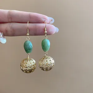 Close-up of vintage gold dangle earrings featuring green resin beads and hollow spheres