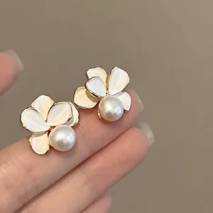 Close-up of 18k gold plated flower pearl stud earrings featuring white enamel petals