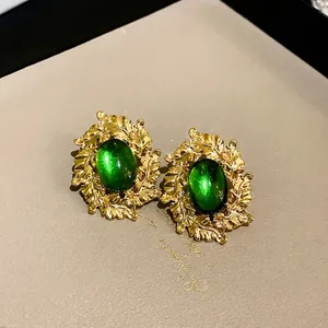 Vintage-style gold leaf earrings featuring emerald green oval gemstones and intricate textures