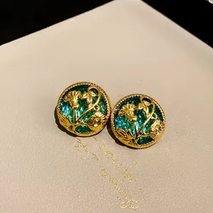 Close-up of elegant vintage style gold floral stud earrings with emerald green background