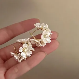 Dettaglio di eleganti orecchini a cerchio con fiori 3D bianchi, perle e zirconi