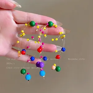 Dettaglio di orecchini colorati con nappe in perle di resina e fili sottili trasparenti