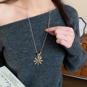 Close-up detail of a gold flower necklace with tiger eye beads worn on a grey sweater.