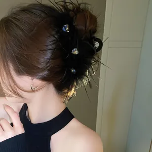 Elegant black feather hair claw clip with rhinestones worn on a brunette bun.
