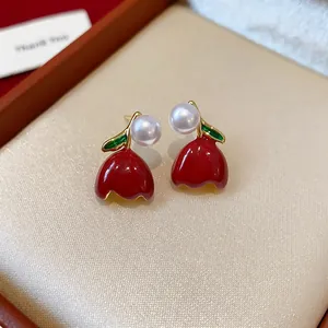 Close-up detail of red enamel tulip earrings with pearls and green leaves accents