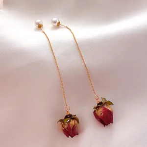 Elegant detail shot of long gold-plated earrings with pearls and real dried rose buds