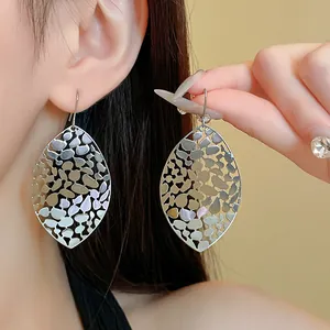 Detail shot of elegant silver hollowed leaf dangle earrings on an Asian model's ear.