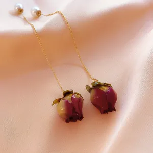 Close-up detail of romantic preserved rose bud drop earrings with gold chain and pearls.