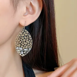 Close-up of minimalist silver hollow metal leaf earrings worn by a female model.