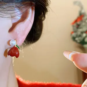 Detailed close-up showing a red enamel apple stud earring with a pearl on a model's ear