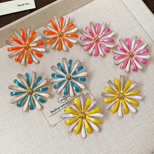 Macro view of colorful enamel daisy stud earrings in orange, pink, blue, and yellow.