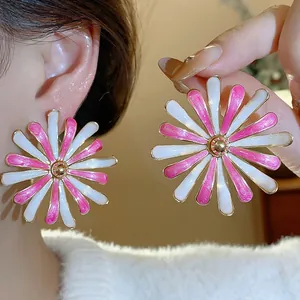 Close-up of pink and white enamel daisy stud earrings with golden accents