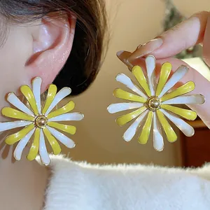 Macro view of stylish yellow and white enamel daisy flower stud earrings worn on ear