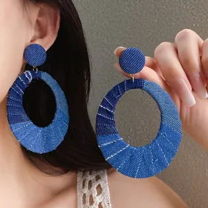 Detail view of stylish large denim fabric oval hoop earrings with textured blue patterns