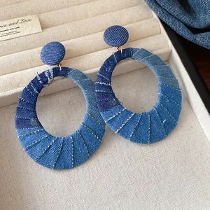 Close-up showing the blue denim fabric texture of oval hoop earrings on a tray