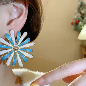 Detailed close-up showing a blue and white enamel flower stud earring worn on a person ear