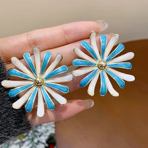 Close-up detail of blue and white enamel flower stud earrings with gold accents