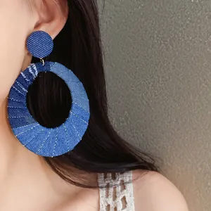 Detailed view of oversized blue denim fabric oval earrings with silver needles