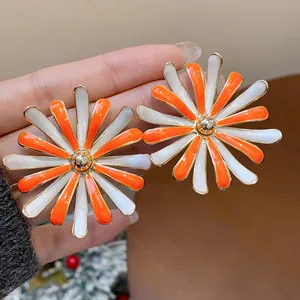 Macro view of vibrant orange and white enamel daisy stud earrings held in hand.