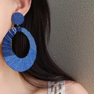 Detailed close-up of stylish blue denim fabric oval hollow earrings worn by model