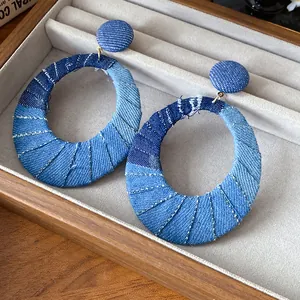 Close-up detail of vintage blue denim fabric oval hoop earrings with silver needle studs.