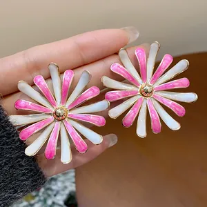 Macro view of fashionable pink and white enamel flower stud earrings held in hand for detail