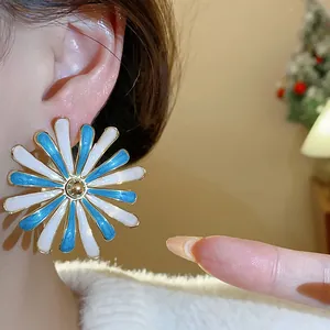 Detailed macro view of a blue and white enamel daisy flower earring worn on ear