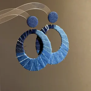 Close-up of large denim hoop earrings with vintage patchwork fabric and white stitching.