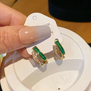 Close-up view of gold-plated geometric earrings featuring green enamel and clear cubic zirconia stones.