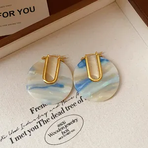Macro detail of retro U-shaped earrings featuring blue marbleized acetic acid pattern discs.