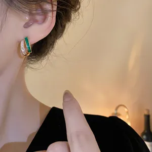 Close-up of elegant gold geometric hoop earrings with green enamel and zircons.