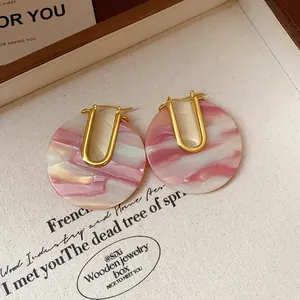 Close-up of vintage U-shaped gold earrings featuring marbled pink acetate round discs