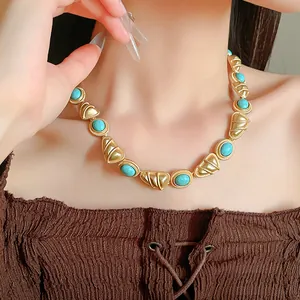 Gros plan d'un collier doré de style vintage avec des pierres turquoises sur modèle.
