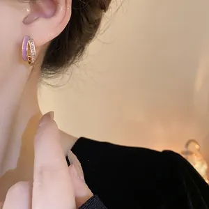 Close-up of gold-plated geometric earrings with zircon and purple enamel detail