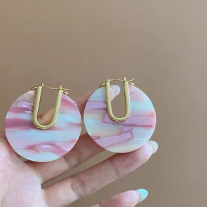 Detail view of U-shaped acetate earrings with pink marble pattern and 18k gold plating.