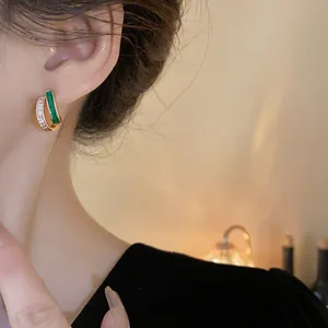 Close-up of elegant gold plated geometric stud earrings with green and clear stones