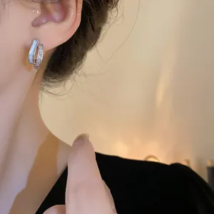 Close-up detail of geometric silver hoop earrings with zircon stones worn by a model