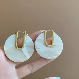 Close-up of retro 18k gold plated U-shaped earrings with white marbled acetate disc detail