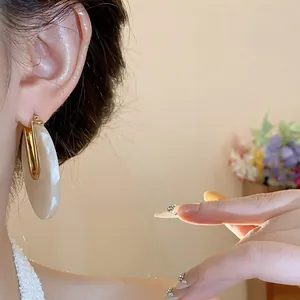 Macro view of 18k gold plated U-shaped statement earrings with beige acetate marble texture.