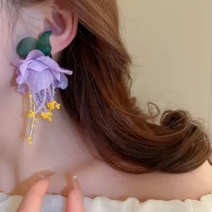 Gros plan d'une boucle d'oreille fleur en tissu mauve avec de longs glands perlés fins