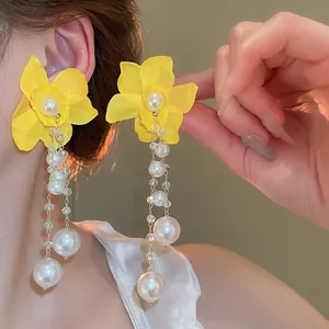 Détail des boucles d'oreilles fleurs en tissu jaune avec glands de perles et cristal.