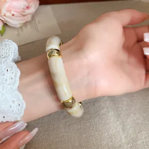 Vista detallada de una elegante pulsera de acrílico jaspeado con cuentas doradas en la muñeca