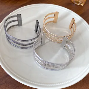 Detail view of multi-layered metal open bracelets in gold, silver, and black finish