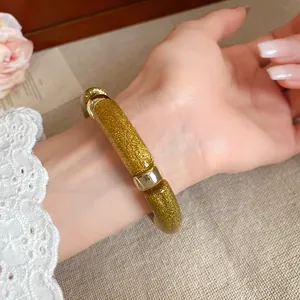 Vista detallada de una pulsera de acrílico con purpurina dorada en la muñeca