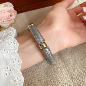 Vista detallada de una pulsera de acrílico gris brillante con elegantes detalles dorados