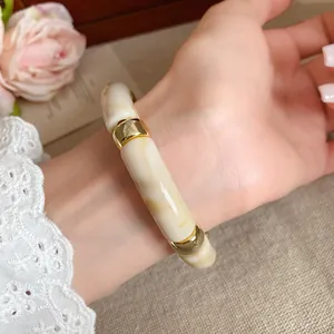 Detalle de una pulsera de acrílico jaspeado crema con adornos dorados en la muñeca